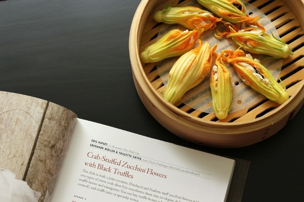 overhead view of zucchini blossoms in a bamboo steamer basket next to an open book