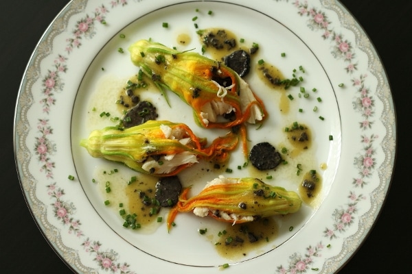 overhead view of three stuffed zucchini flowers drizzled with sauce on a china plate