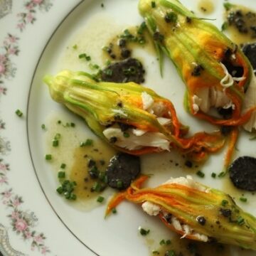 overhead closeup of stuffed zucchini flowers with black truffles on a china plate