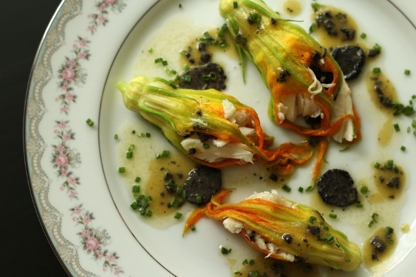 overhead closeup of stuffed zucchini flowers with black truffles on a china plate