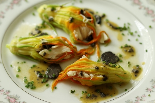 three steamed stuffed zucchini blossoms with sliced black truffles on a white china plate