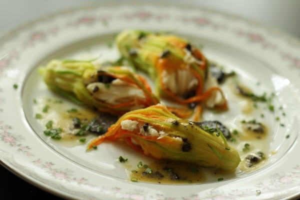 three stuffed zucchini flowers drizzled with sauce on a fine china plate