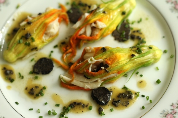 a white china plate with stuffed zucchini flowers, sliced black truffles, and vinaigrette drizzle
