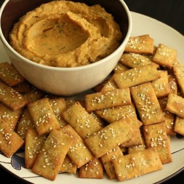 a bowl with a tan colored dip surrounded by rectangular crackers on a plate