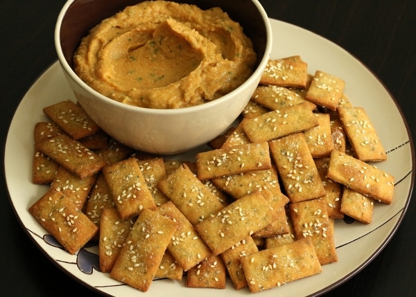 a bowl with a tan colored dip surrounded by rectangular crackers on a plate