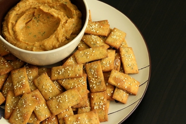 overhead view of a pile of rectangular crackers surrounding a bowl of dip