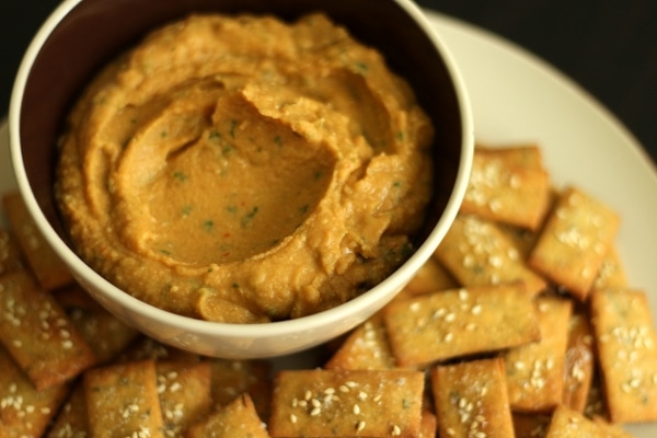 A closeup of a smooth tan colored dip in a bowl surrounded by crackers