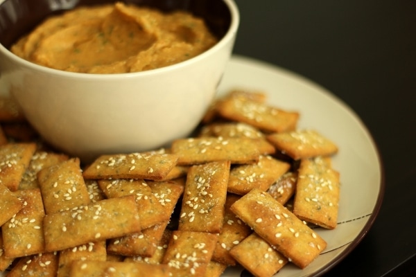 a plate of rectangular crackers next to a bowl of dip