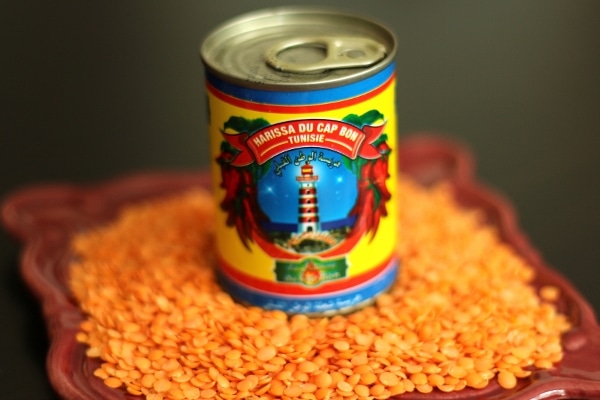 a can of harissa on a plate surrounded by uncooked red lentils