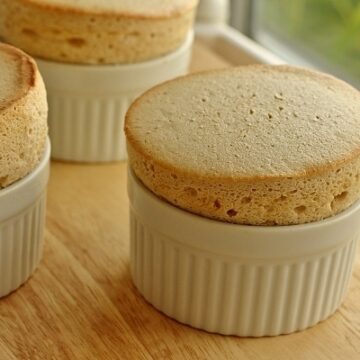 a closeup of three souffles in white ramekins on a wooden board