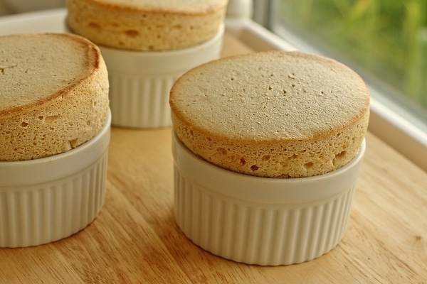 a closeup of three souffles in white ramekins on a wooden board