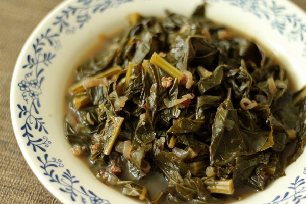 a shallow bowl piled high with braised collard greens in broth