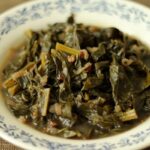 a white shallow bowl with blue trim filled with braised collard greens with broth