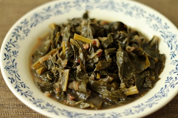 a white shallow bowl with blue trim filled with braised collard greens with broth