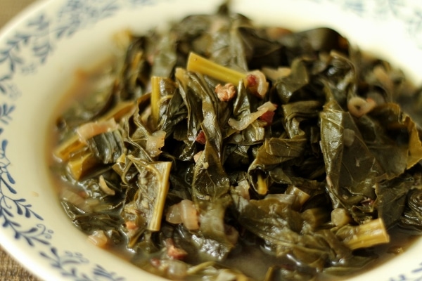 a closeup of braised collard greens in a murky broth in a shallow bowl