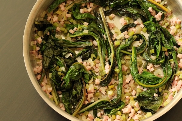 overhead view of a round metal pan filled with diced ham and cooked Swiss chard