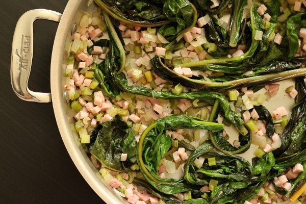 overhead closeup of a metal All Clad pan filled with diced ham and cooked Swiss chard