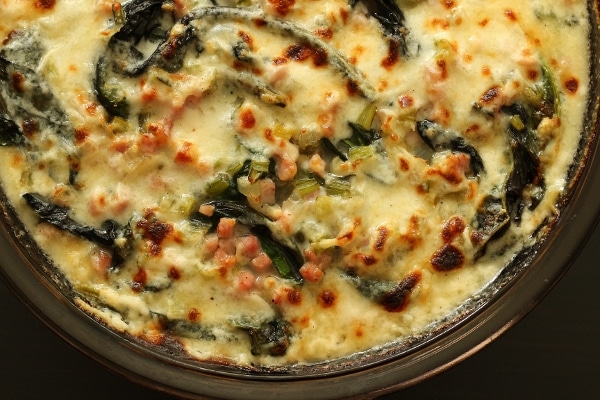 a round baking dish filled with creamy gratin of Swiss chard and diced ham