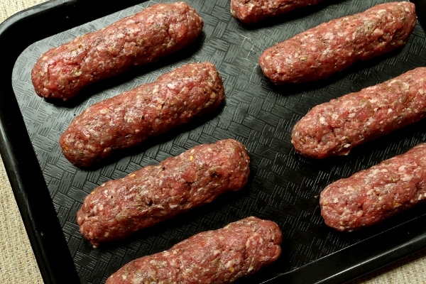 raw skinless sausages arranged on a black tray