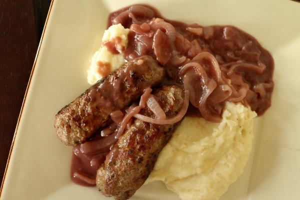 overhead view of a square plate with mashed potatoes, skinless sausages, and onion gravy