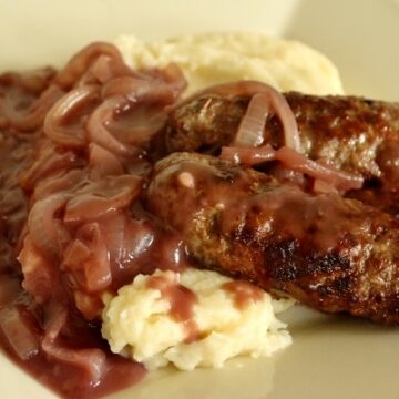 two skinless sausages over mashed potatoes with onion gravy over the top