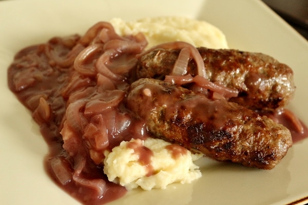 two skinless sausages over mashed potatoes with onion gravy over the top