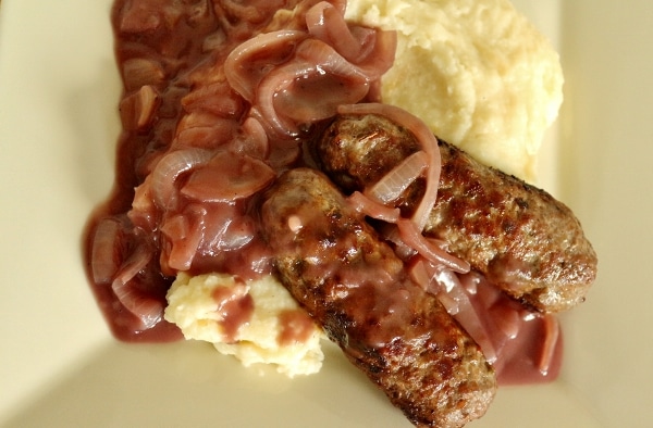 two cooked skinless sausages over mashed potatoes with red wine onion gravy