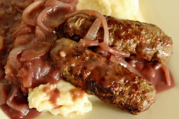 a closeup of two cooked skinless sausages over mashed potatoes with onion gravy