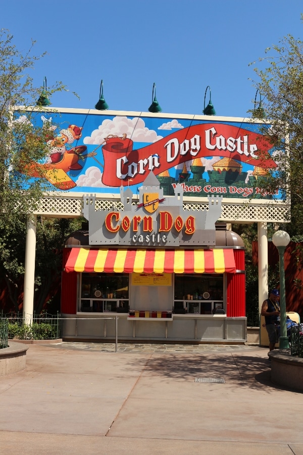 A sign that says Corn Dog Castle over a small building with a striped awning