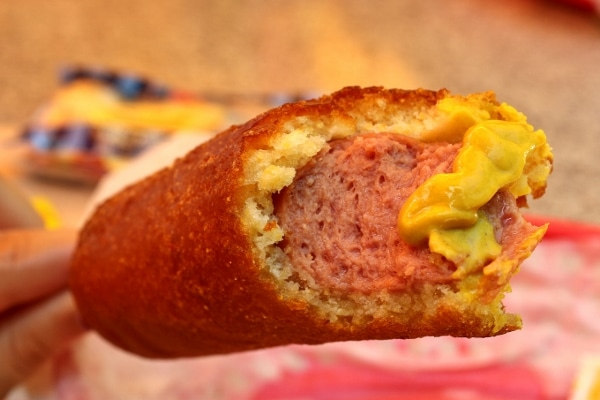 A closeup of a half-eaten corn dog with yellow mustard on it