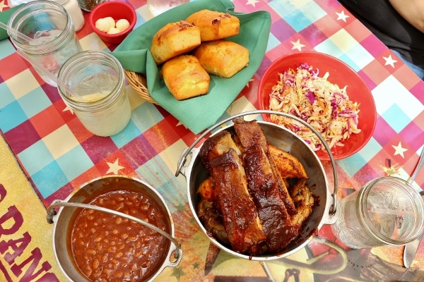 overhead view of buckets of ribs and beans, a bowl of coleslaw and basket of cornbread