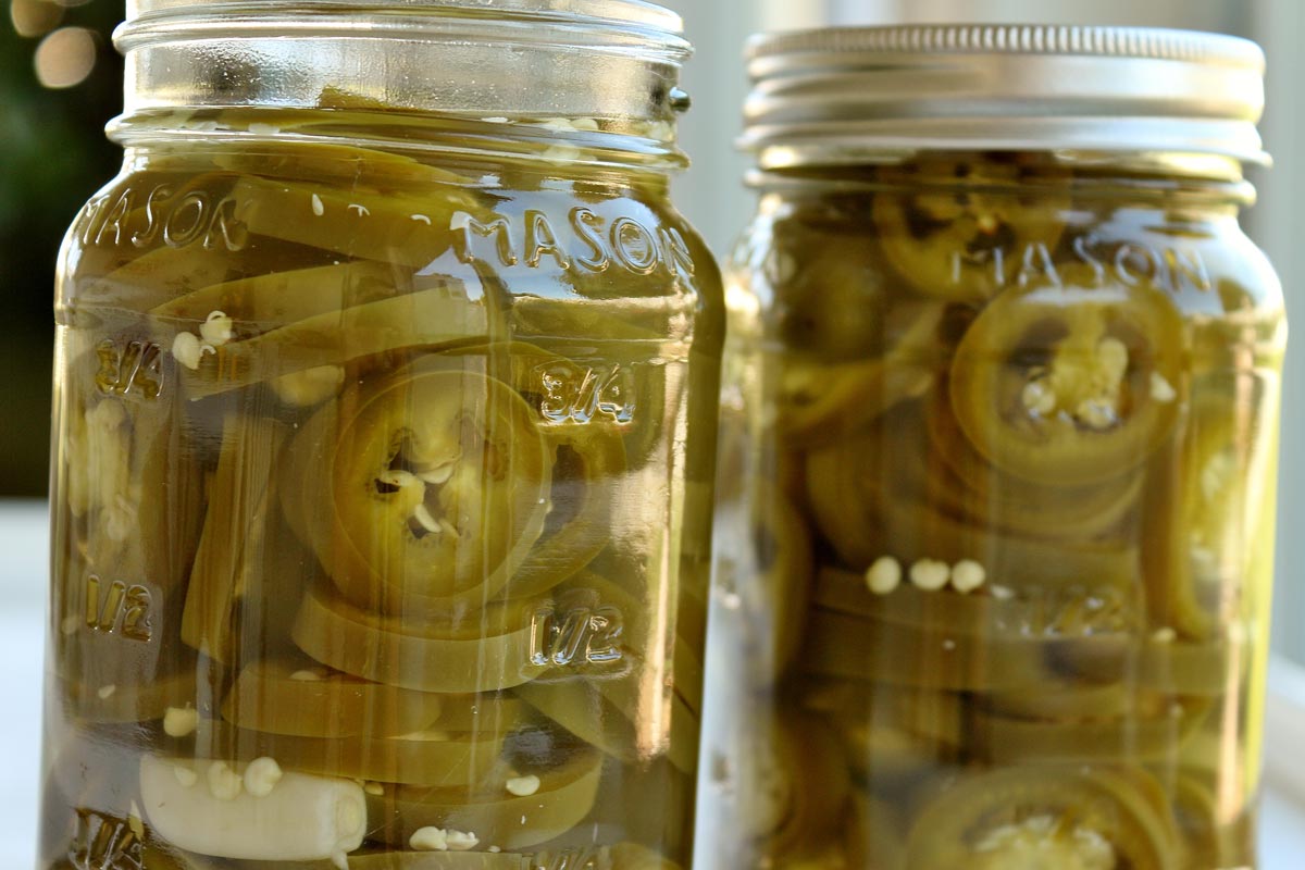 A closeup of 2 jars of pickled jalapenos side by side.