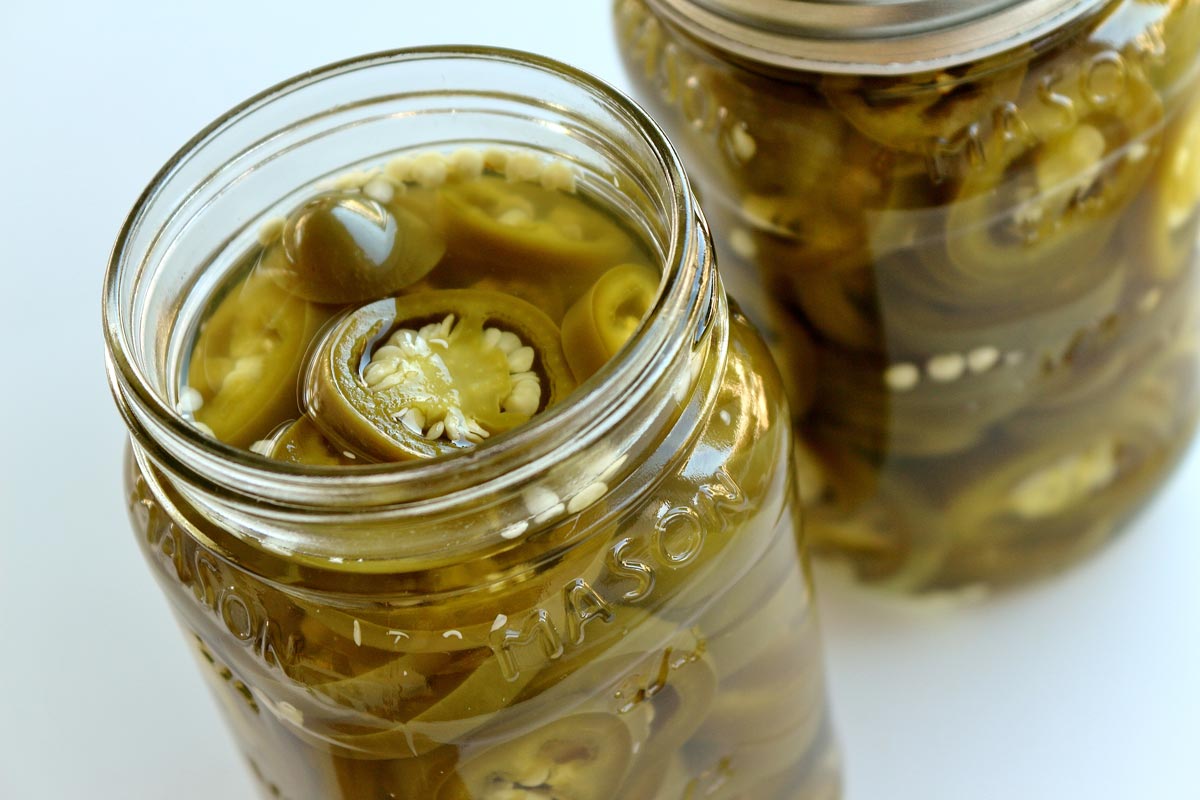 A close up view of 2 jars of pickled jalapeno peppers.