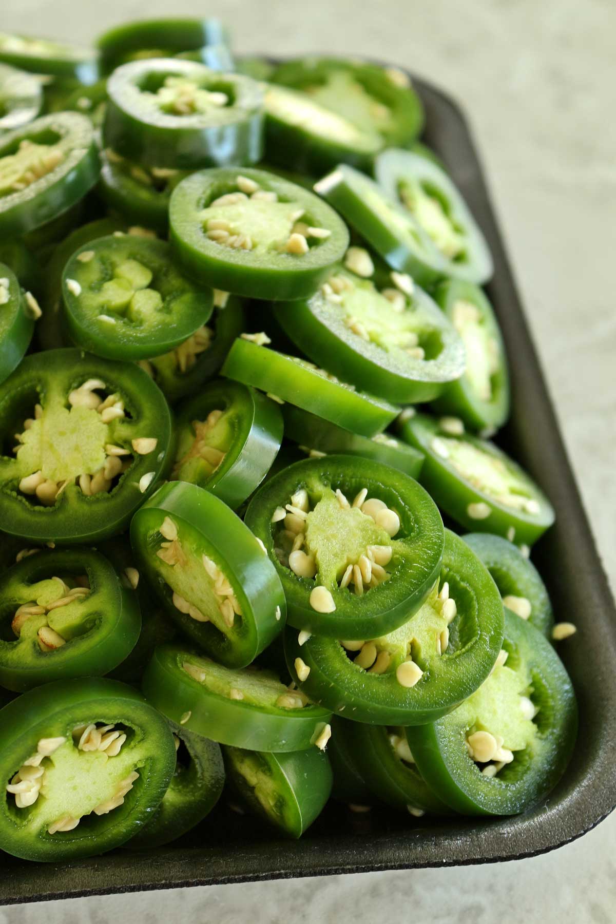 Sliced jalapeno peppers piled high on a black cafeteria tray.