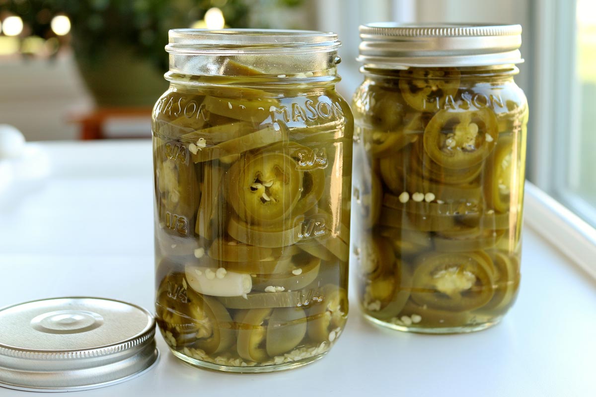 Two jars of homemade pickled jalapenos, one without a lid.