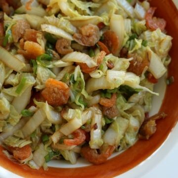 overhead view of a brown and white bowl filled with stir-fried cabbage with dried shrimp