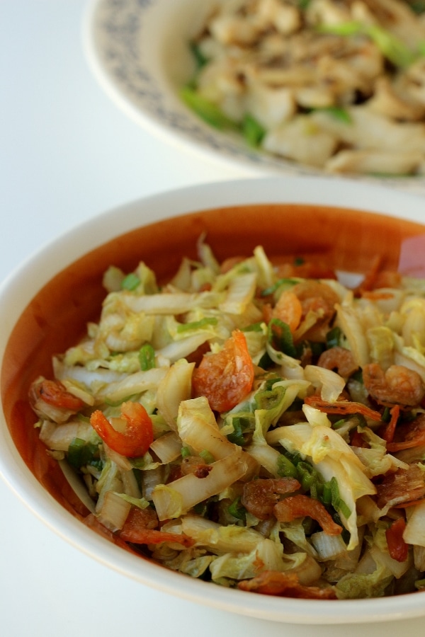 closeup of stir-fried cabbage with dried shrimp in a brown and white bowl