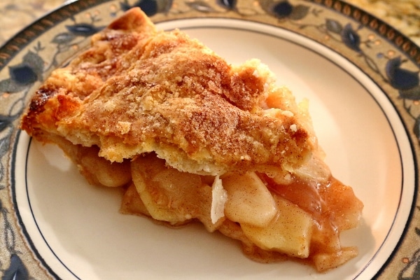 closeup of a slice of apple pie on a plate with floral decorations around the edge