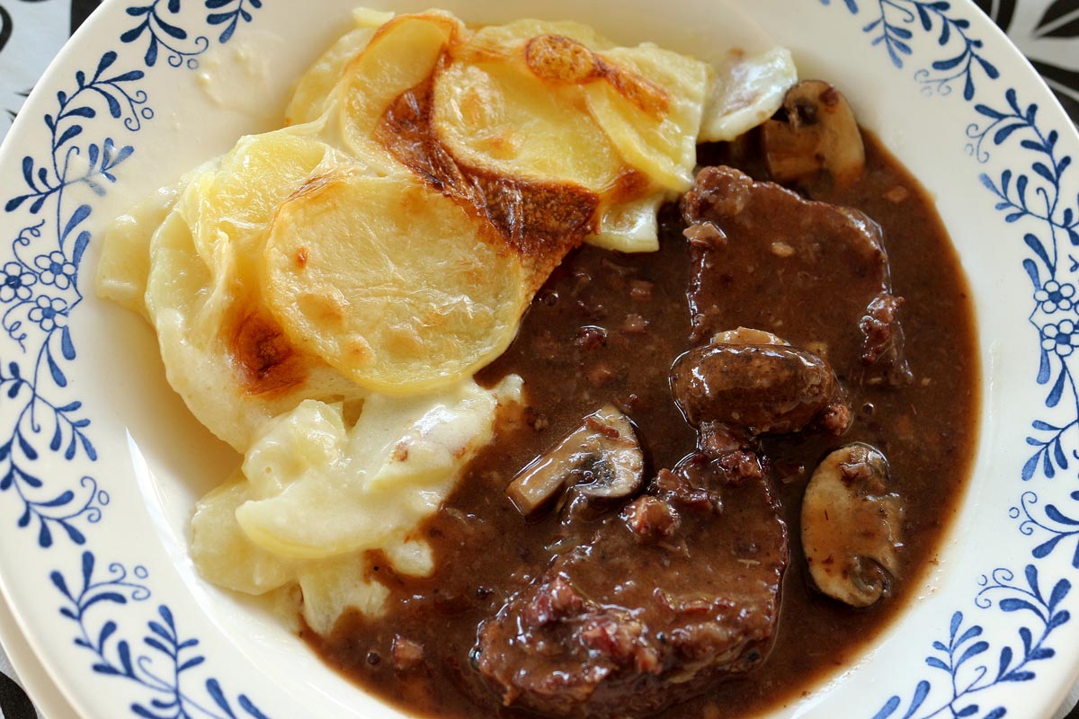 A shallow white bowl filled with beef bourguignon stew and potato gratin.