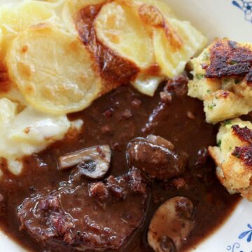 Beef bourguignon with baguette dumplings and potatoes dauphinoise in a wide bowl.