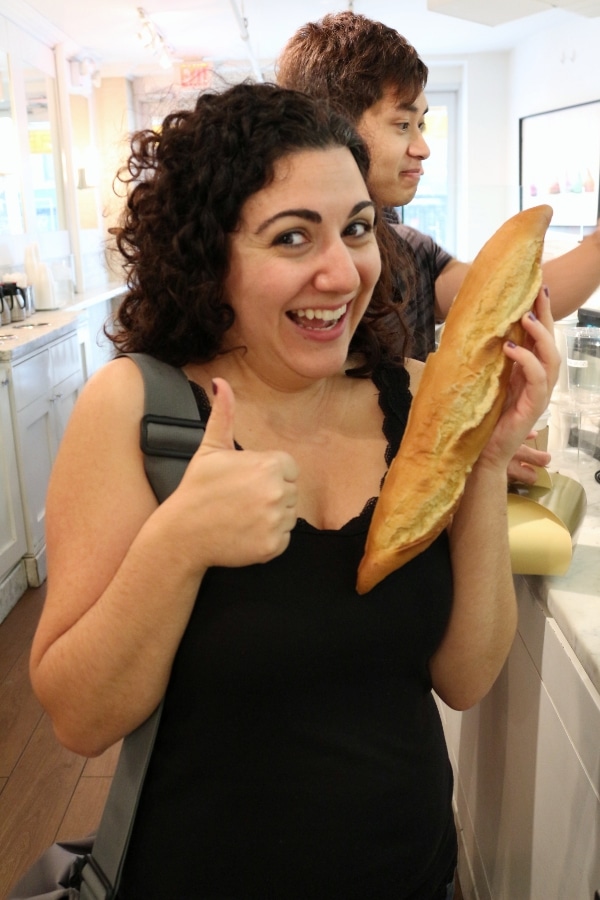 A person giving a thumbs up and holding a fake baguette