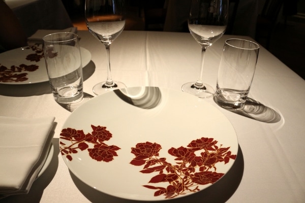 a white plate with red flowers on a white tablecloth covered table