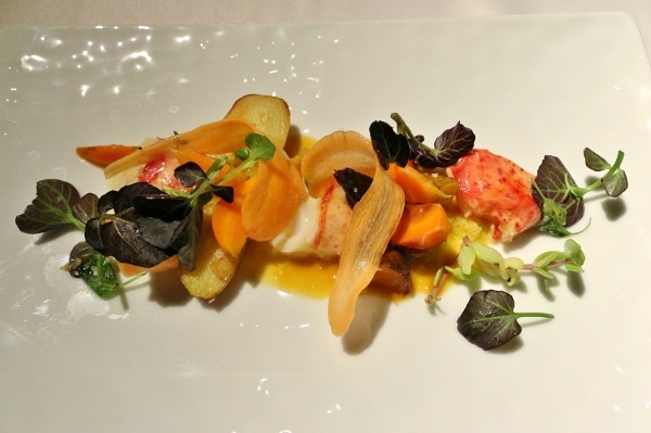 a plate of colorful food with lobster pieces and vegetables