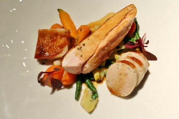 A plate of chicken with round white sausage and colorful vegetables