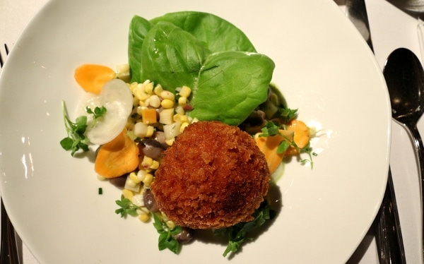 a round fried croquette on a plate with corn and green leaves