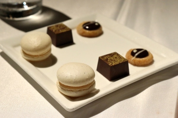 a white square plate with macaron cookies and chocolates on top