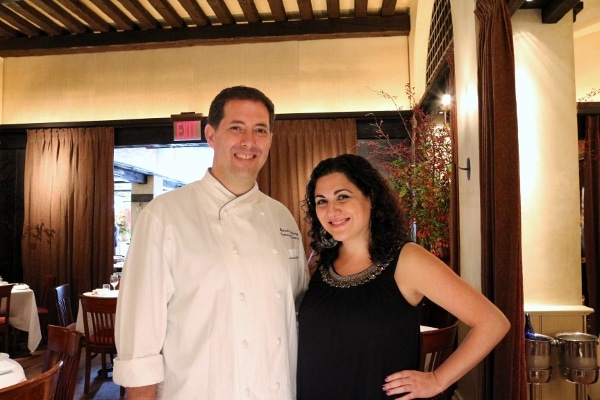 a man in a white chef\'s coat and a woman in a black shirt pose together