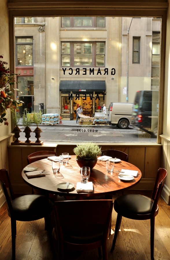 a round wooden restaurant table in front of a window looking out to the street