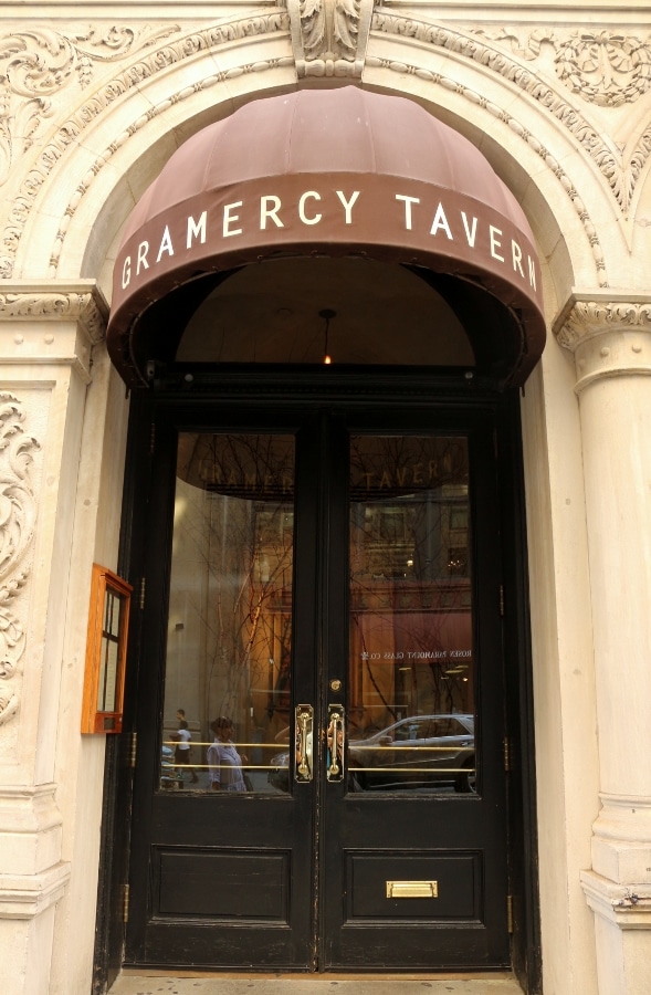 exterior of Gramercy Tavern restaurant with a brown awning over glass double doors