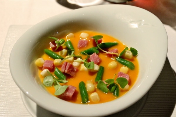 a bowl of orange colored soup with cubes of meat, corn, and green beans